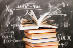 Opened book on a stack in front of a blackboard with mathematical formulas Opened book on a stack in front of a blackboard with mathematical formulas